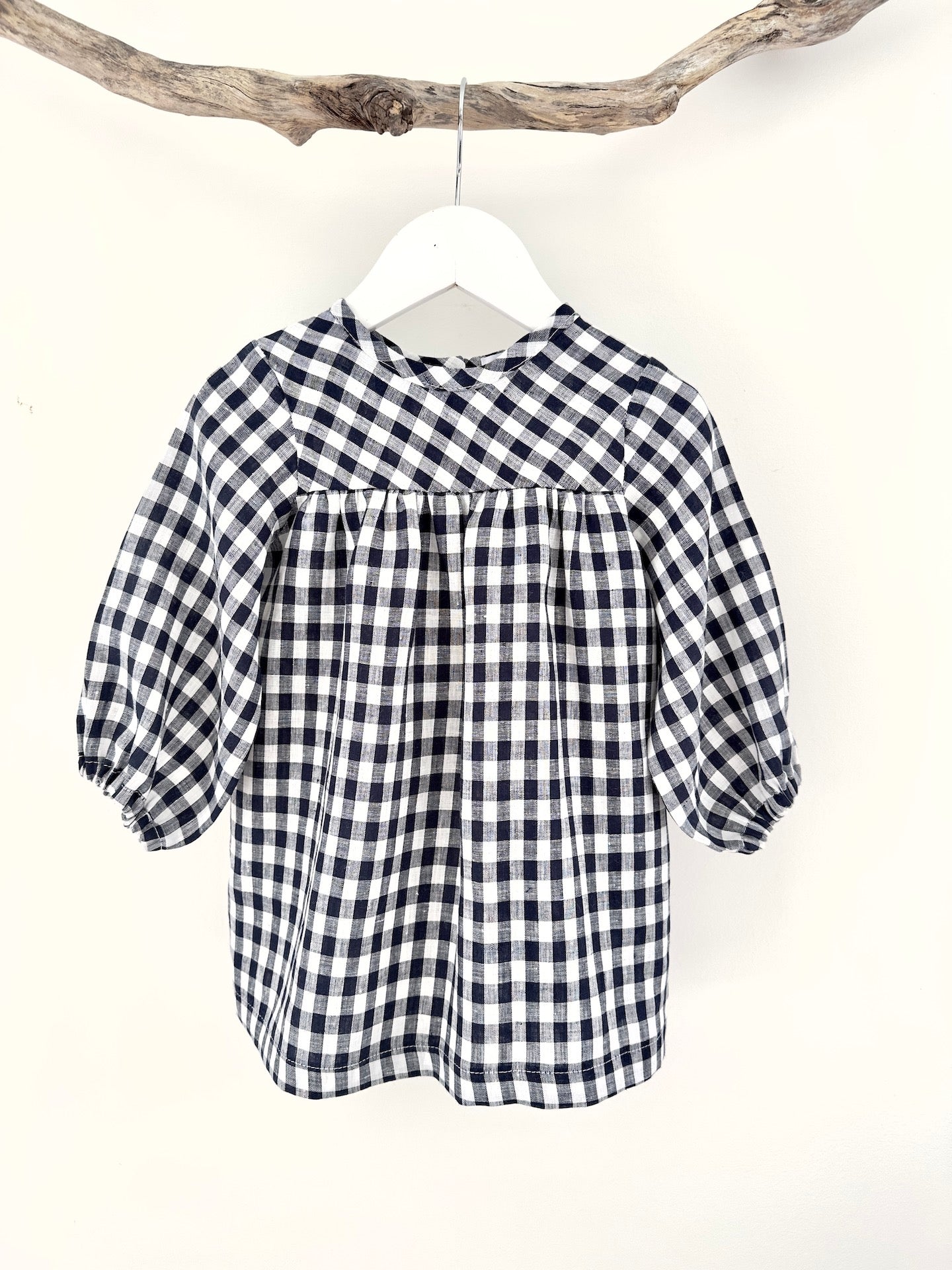 A navy and white checkered long sleeve dress for children, displayed on a hanger.
