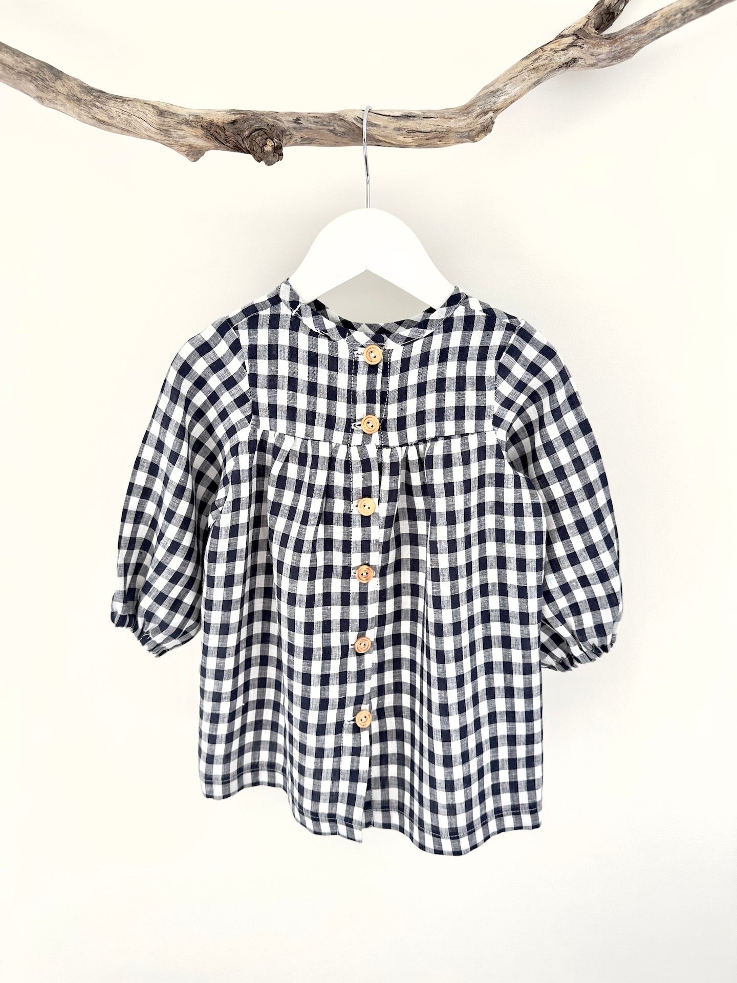 A navy and white checkered long sleeve dress for children, displayed on a hanger.