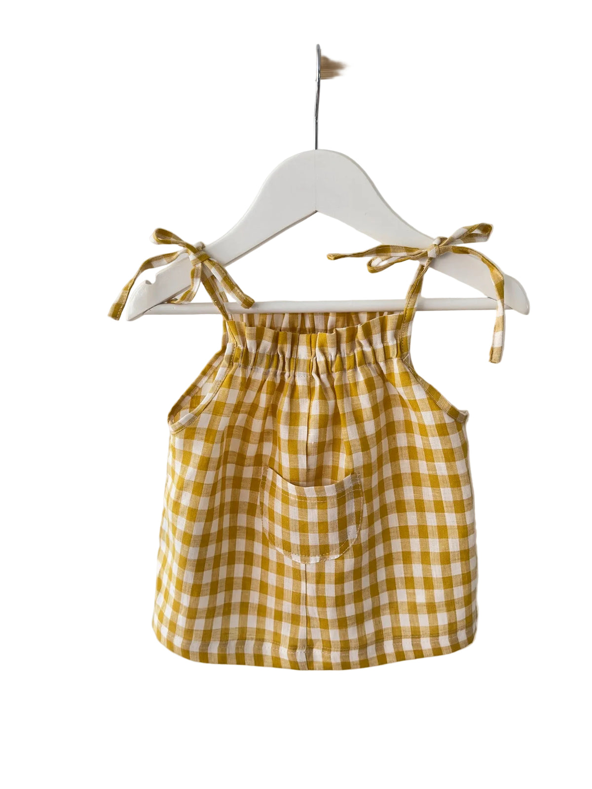 A yellow and white gingham check baby romper with tie-shoulder straps and a front pocket, hanging on a white hanger from a wooden rod against a white wall.